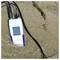 Handheld Seneca meter in shallow water on sand, displaying a reading of 26.5 with cables attached.