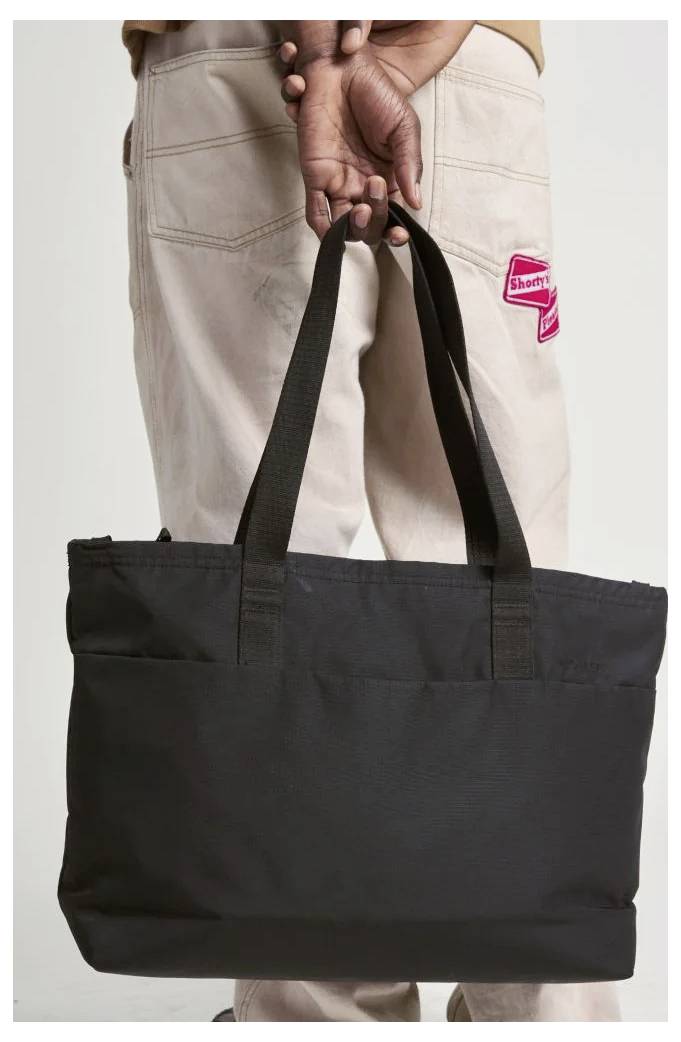 Person holding a large black tote bag by its handles in front of beige pants.