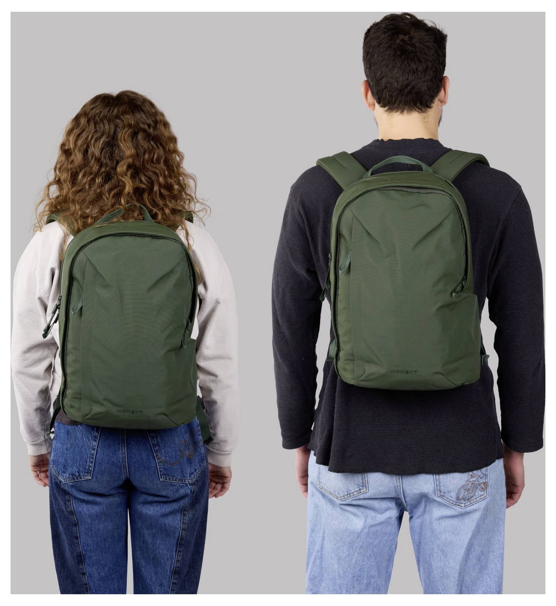 Two people seen from behind wearing green backpacks against a plain gray background.