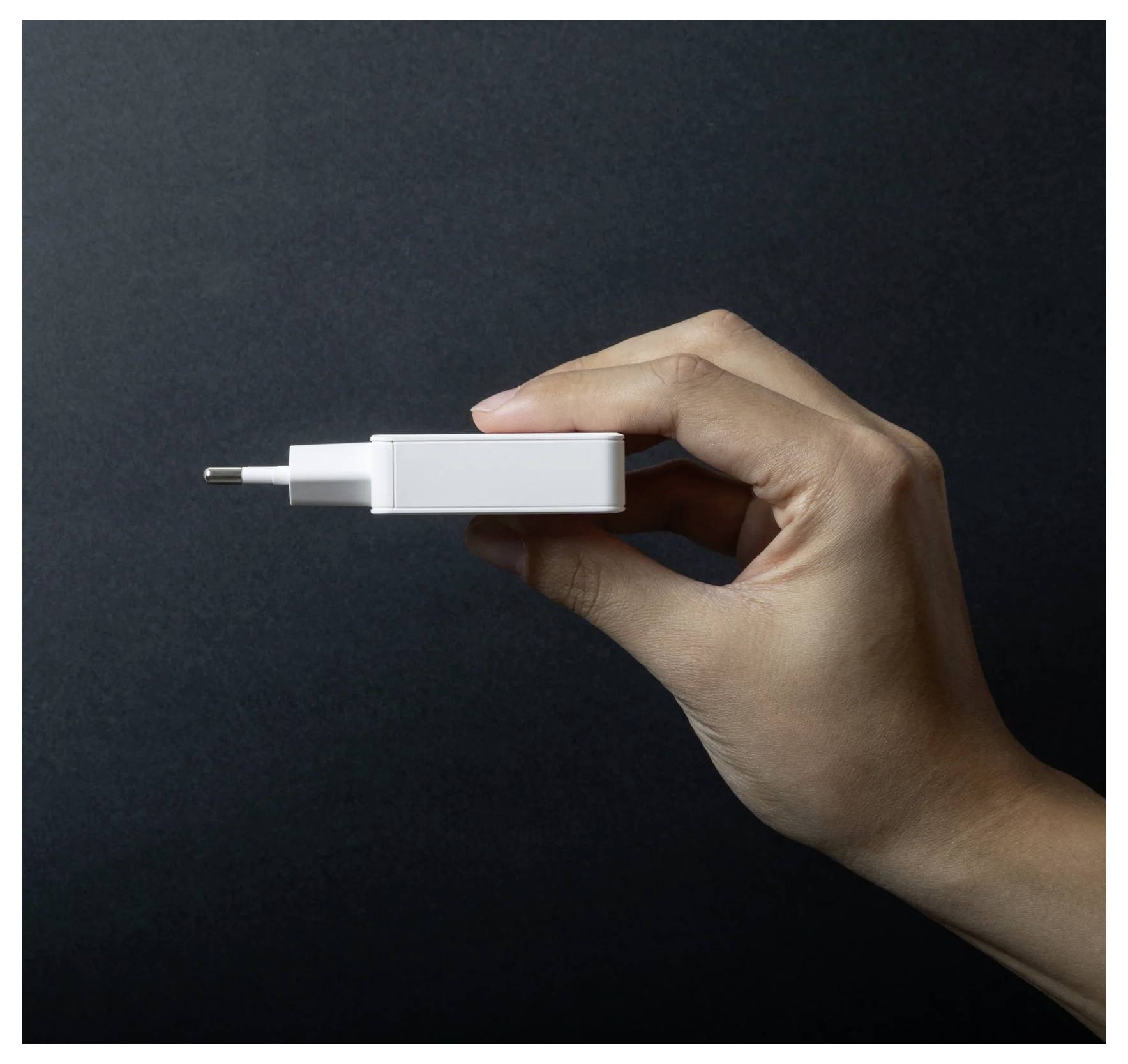 Hand holding a white USB wall charger plug against a dark background, shown in profile.