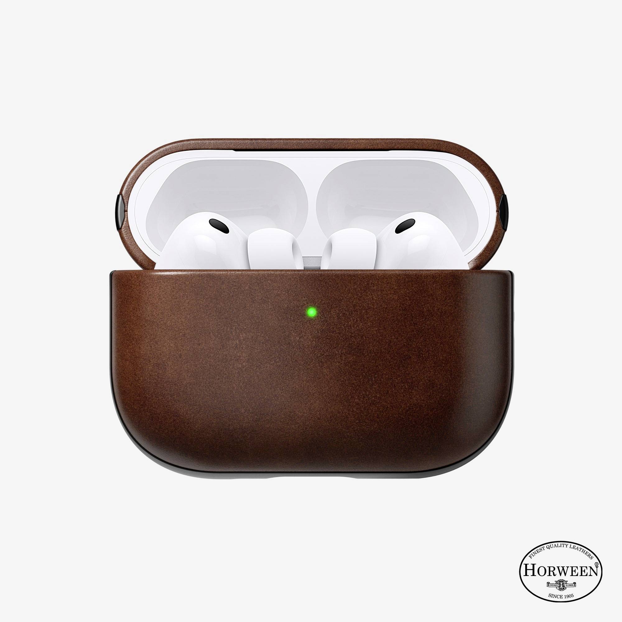 White wireless earbuds in an open brown leather charging case with a green status light on a white background.<br>