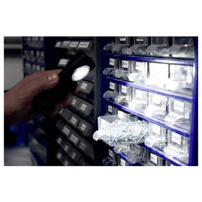 Hand holding a lit flashlight near stacked plastic drawer bins in a storage or hardware area, illuminating a drawer of small parts.