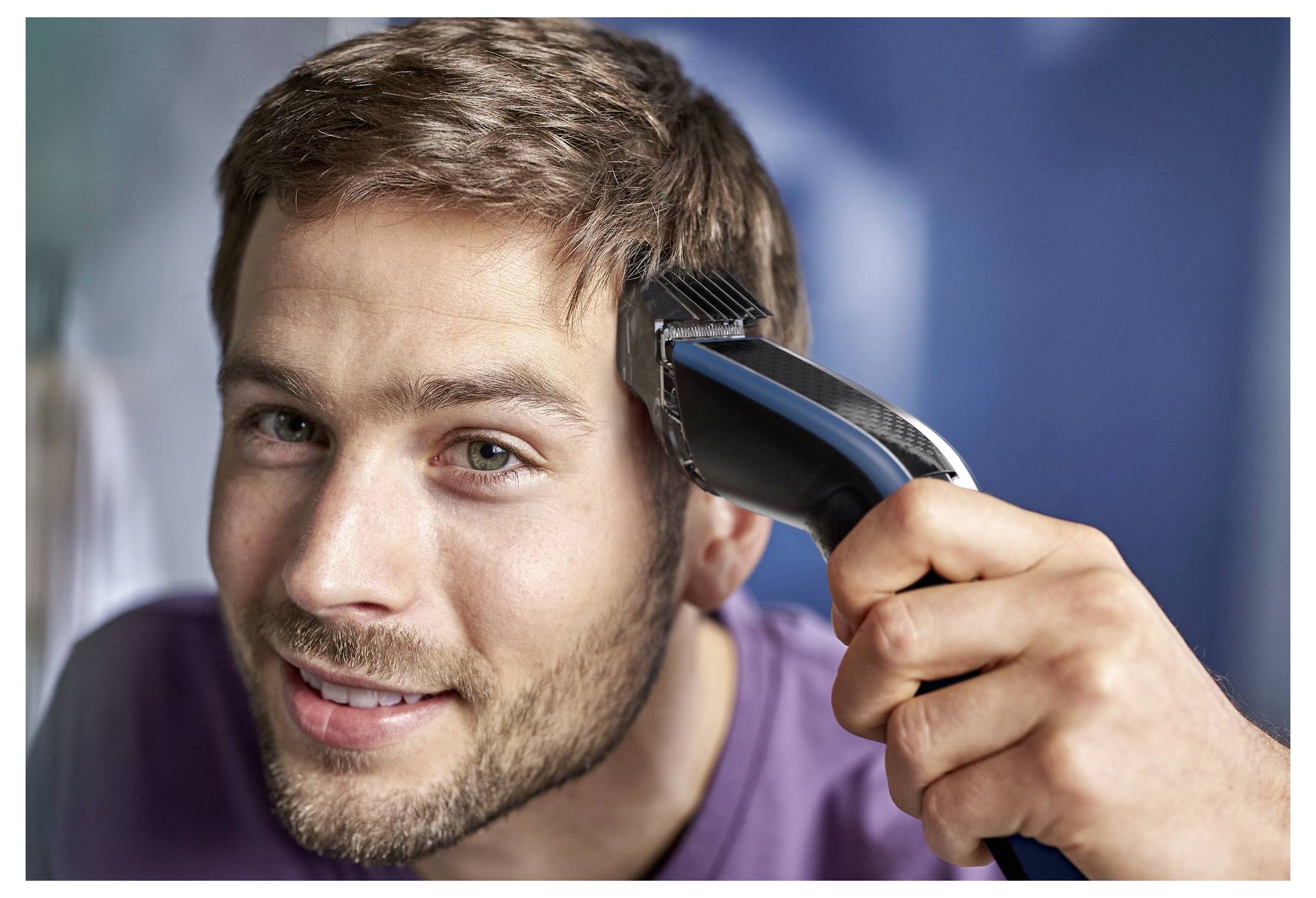 Close-up of a man smiling while having his hair trimmed with electric clippers.