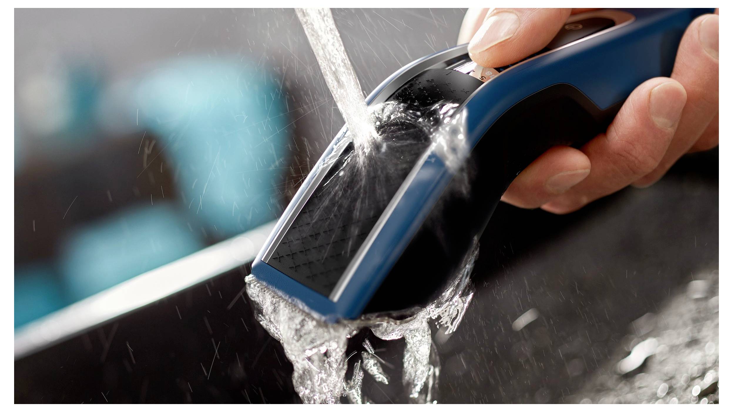 Hand rinsing a blue-and-black electric shaver under running water in a sink, cleaning the device.<br>