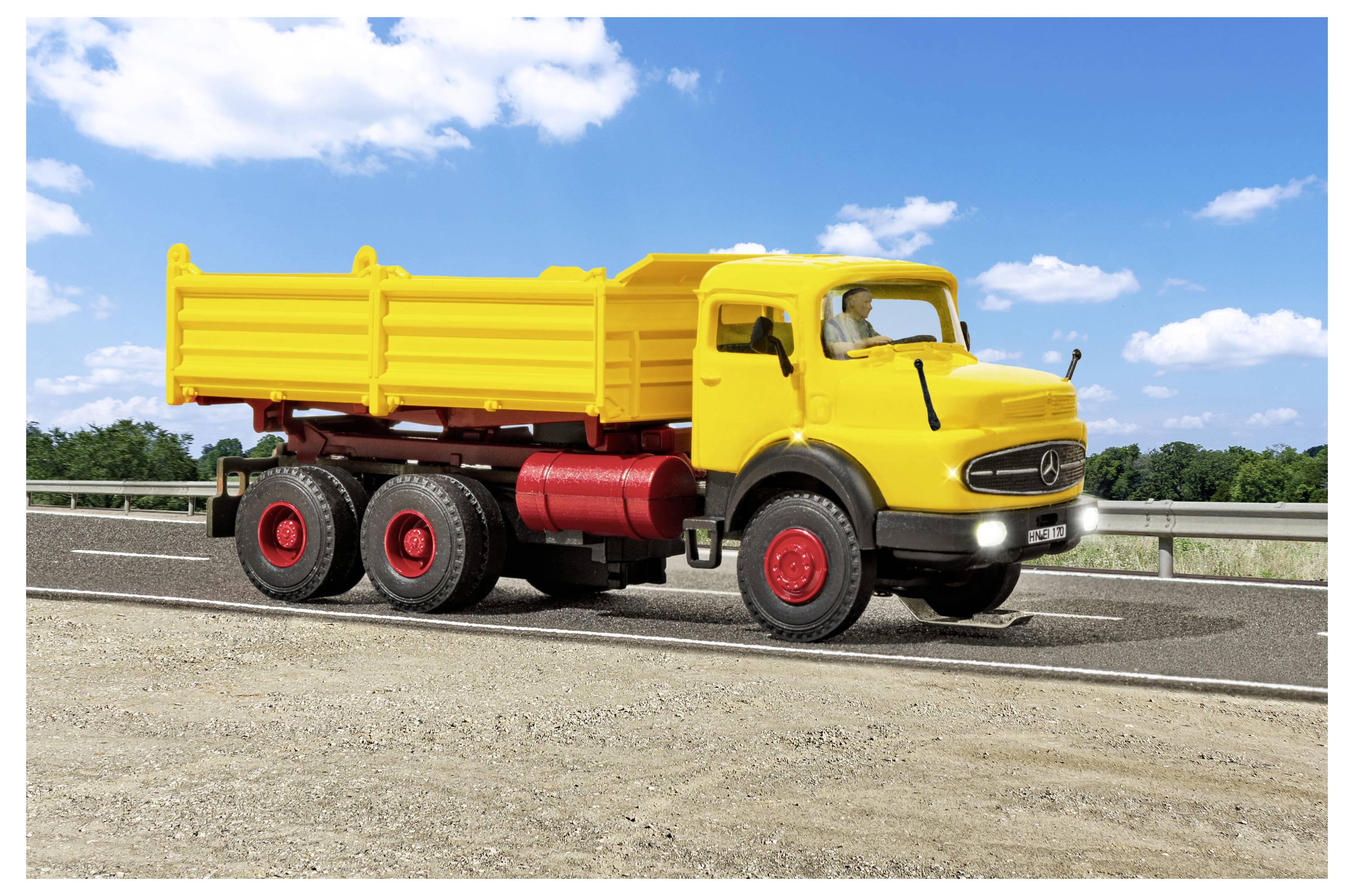 Yellow dump truck driving on a road under a blue sky with clouds.