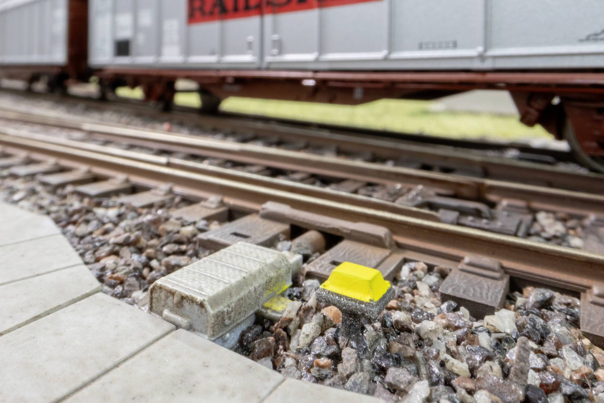 Close-up of railroad tracks with trackside electrical equipment boxes and a passing train blurred in the background.
