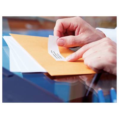 Hands placing a small paper slip into an orange envelope on a glass table, suggesting sending or sealing a message.