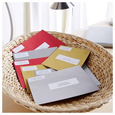 Woven basket holding several addressed envelopes in red, gray, gold, and white on a desk.