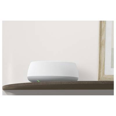 A white, rounded smart device sits on a wooden shelf against a plain wall.<br>