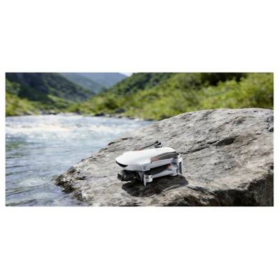 A small white drone rests on a rock beside a river in a mountain valley.
