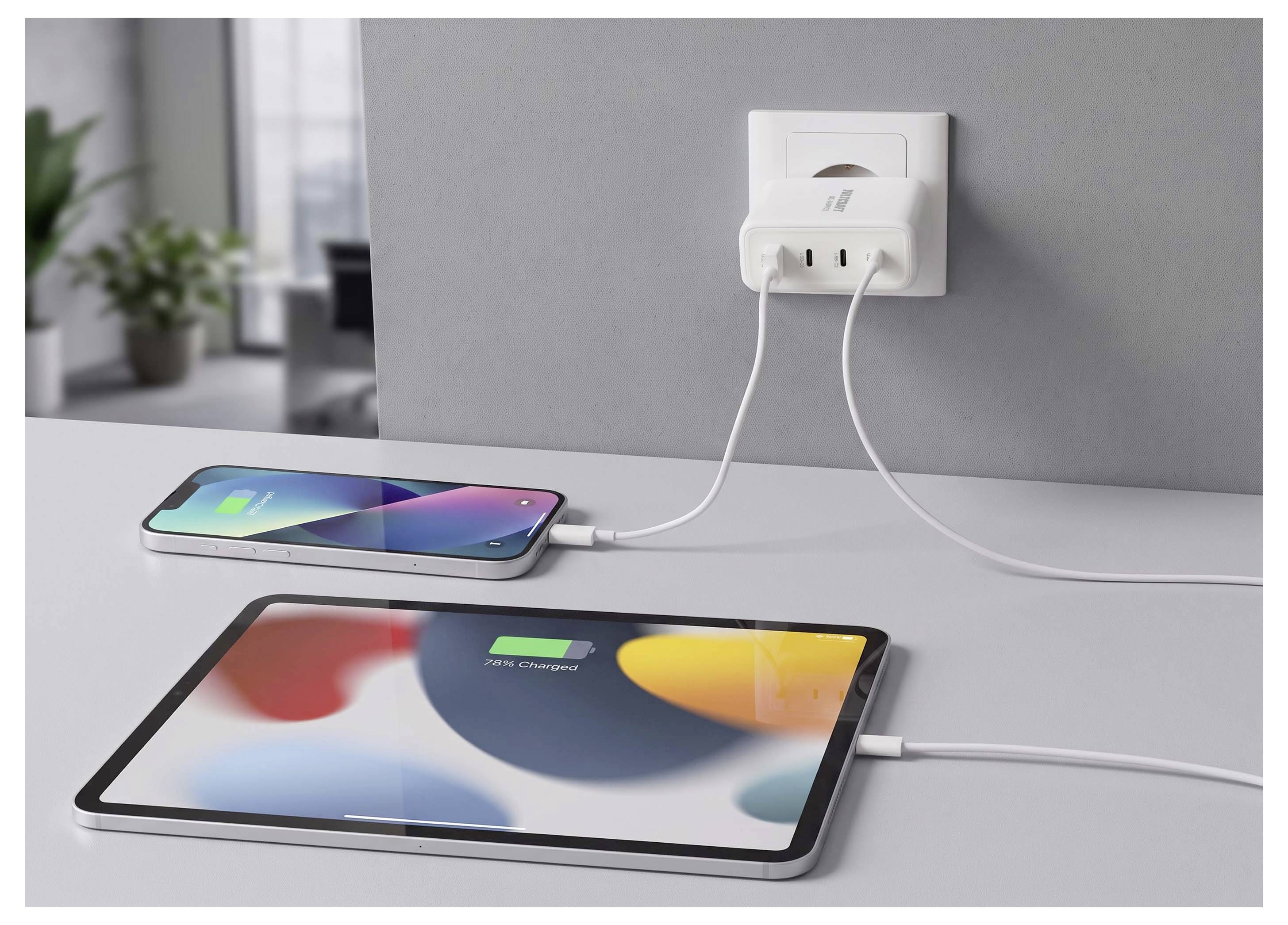 A smartphone and a tablet are plugged in and charging from a wall outlet on a desk.