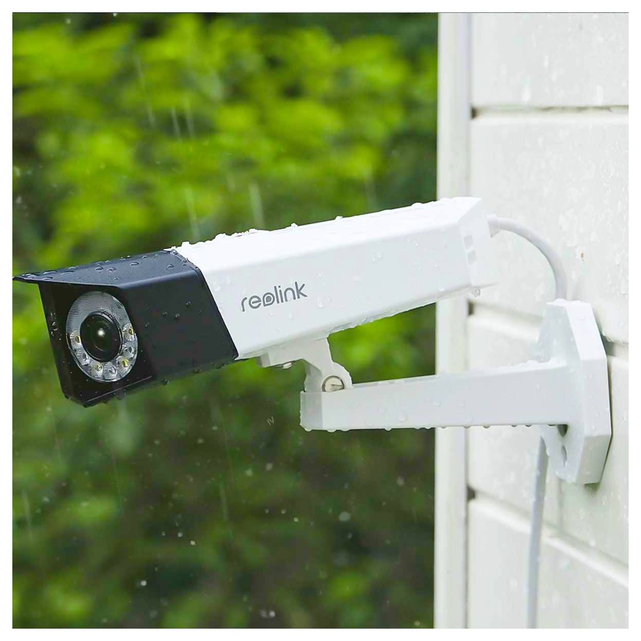 White Reolink security camera mounted on a house exterior, aimed outdoors in the rain.