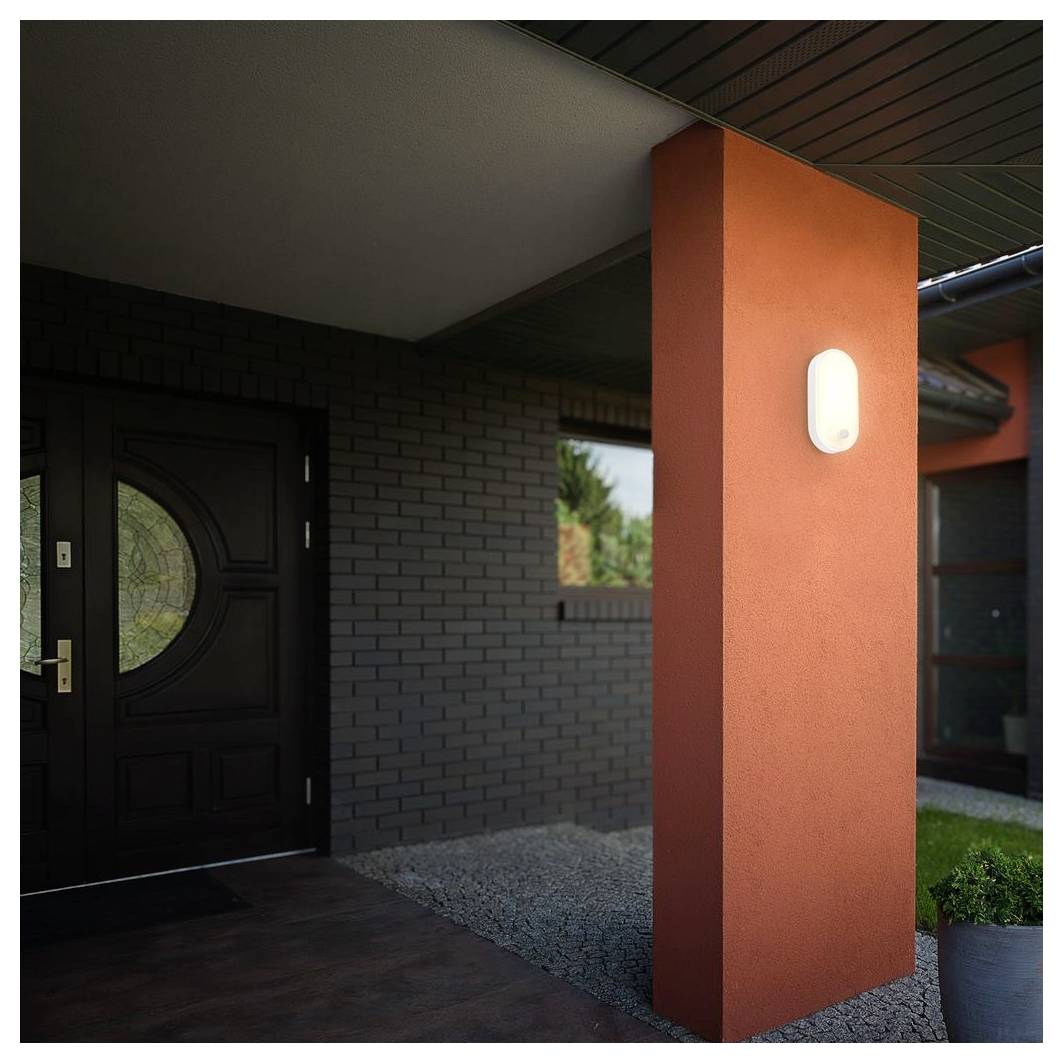 Modern house entryway with a black front door, orange pillar, wall light, and gravel landscaping under a covered porch.