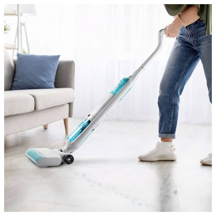 Person vacuuming a bright living room with a cordless stick vacuum beside a sofa.