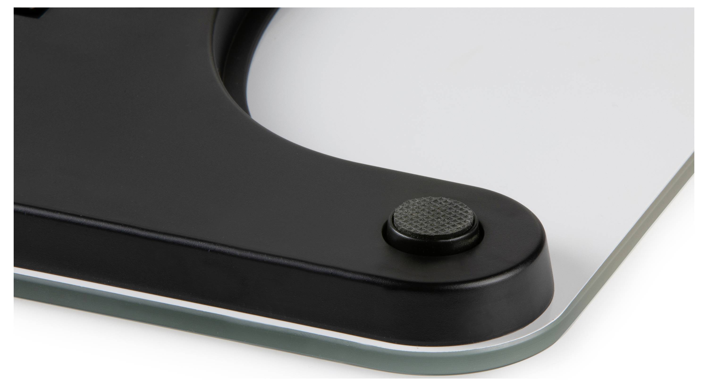 Close-up of a black device corner with a textured round button mounted on a glass surface.<br>