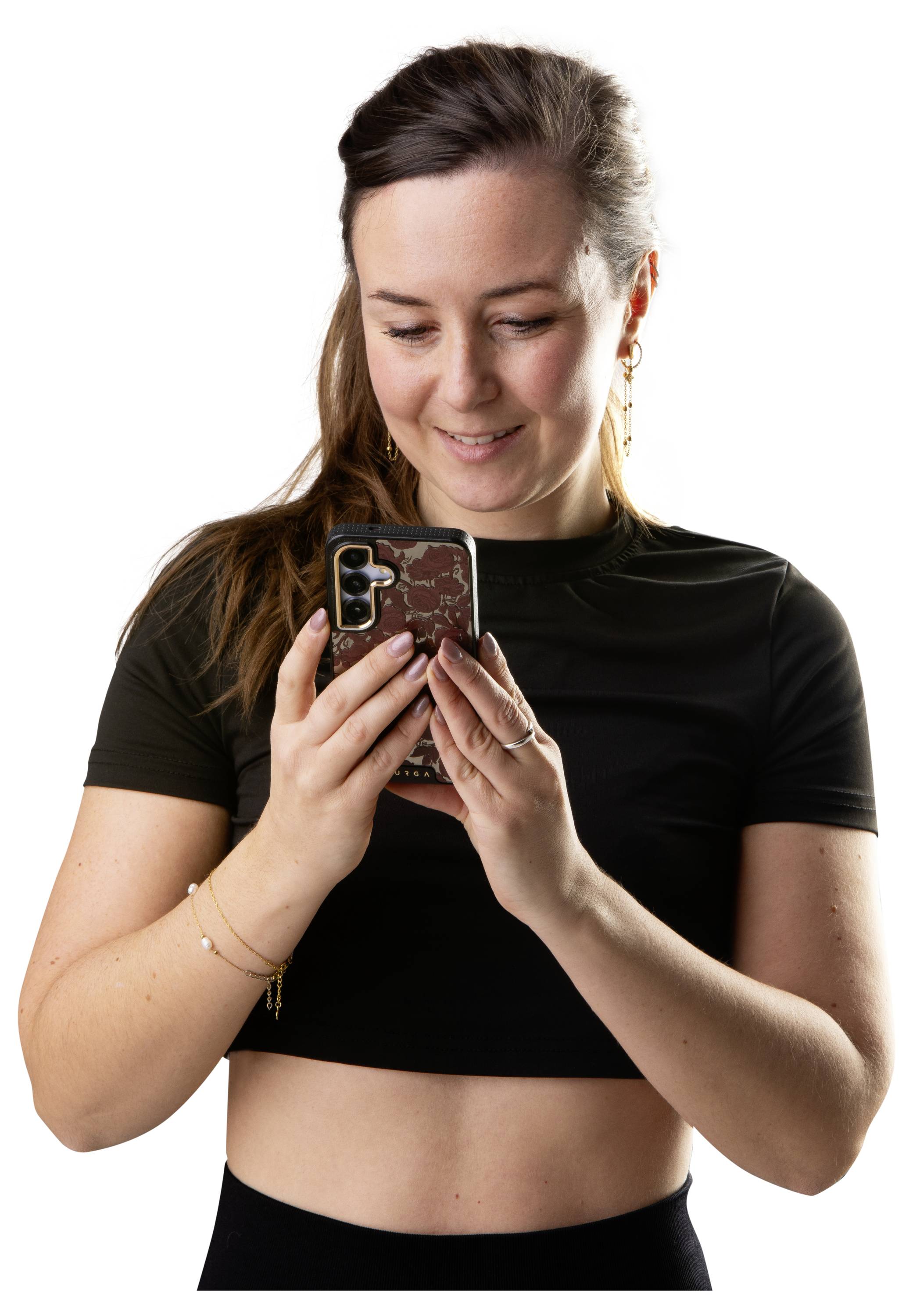 Young woman in a black top smiling while looking down at her smartphone against a white background.