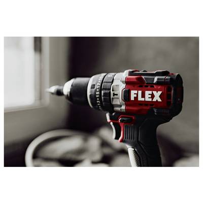 Close-up of a red and black FLEX cordless drill aimed toward a window, with a blurred workshop background.