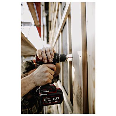 Close-up of a worker using a cordless drill to drive a screw into a wooden wall or frame on a construction site.<br>