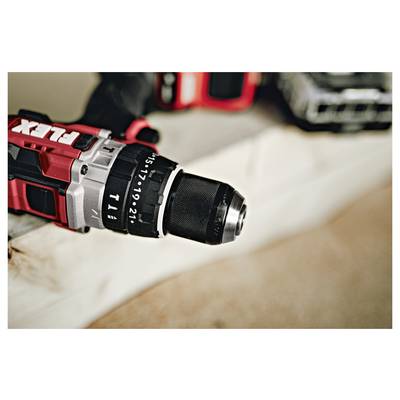 Close-up of a red cordless drill with a black chuck on a work surface, showing the front end and depth markings.