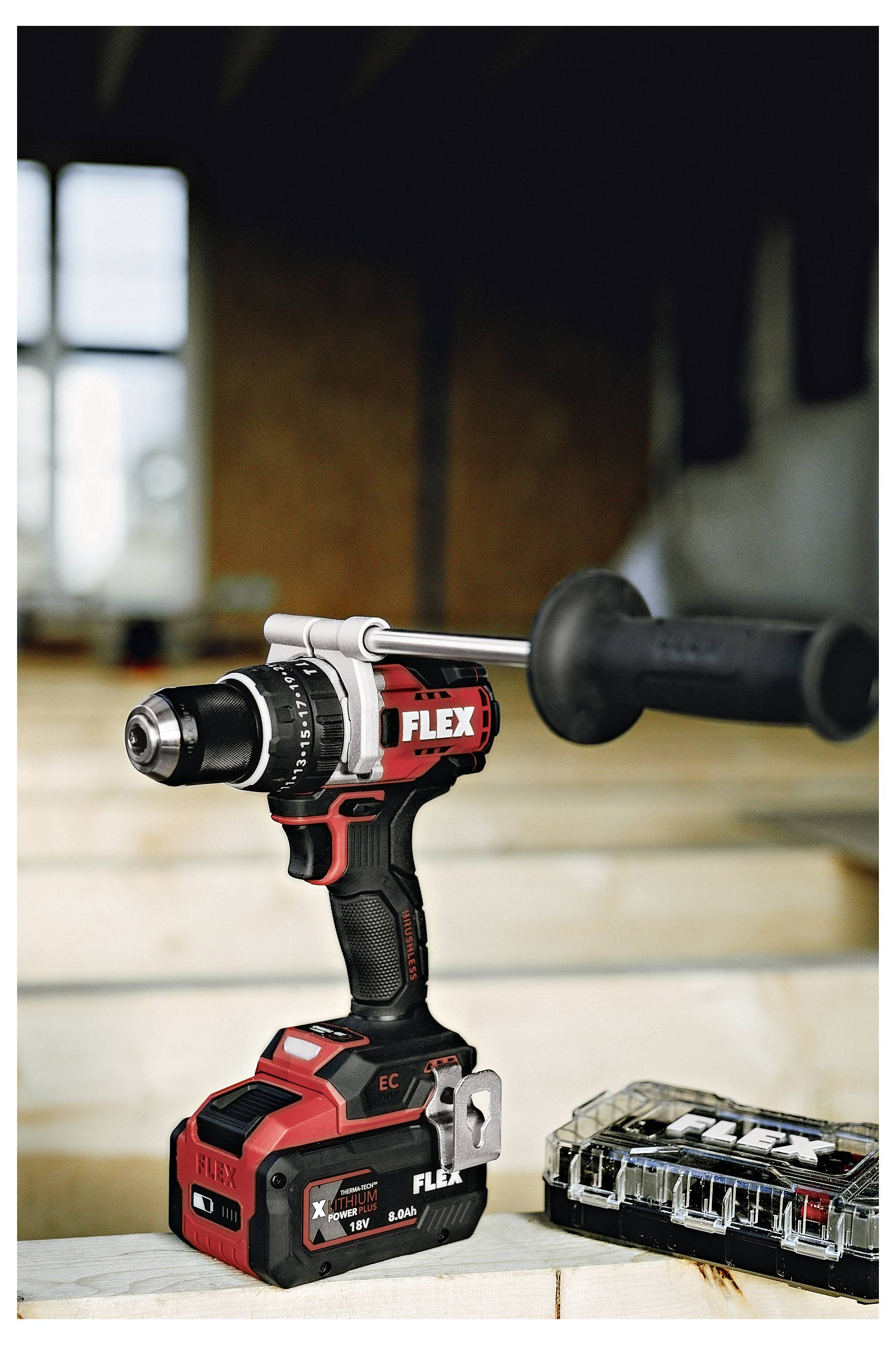Cordless FLEX drill with side handle and battery, standing next to a FLEX drill bit case on a workbench.