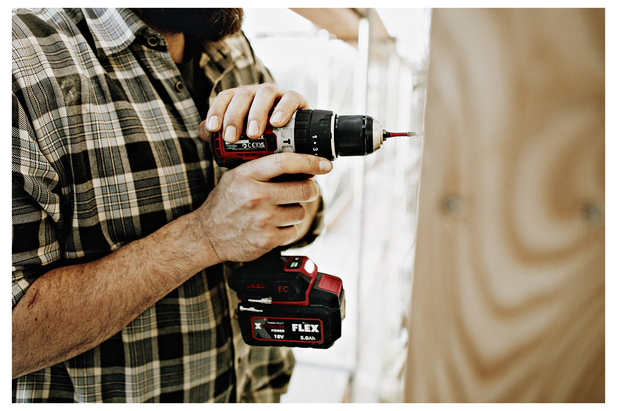 Person using a cordless drill to drive a screw into a wooden board during construction or carpentry work.