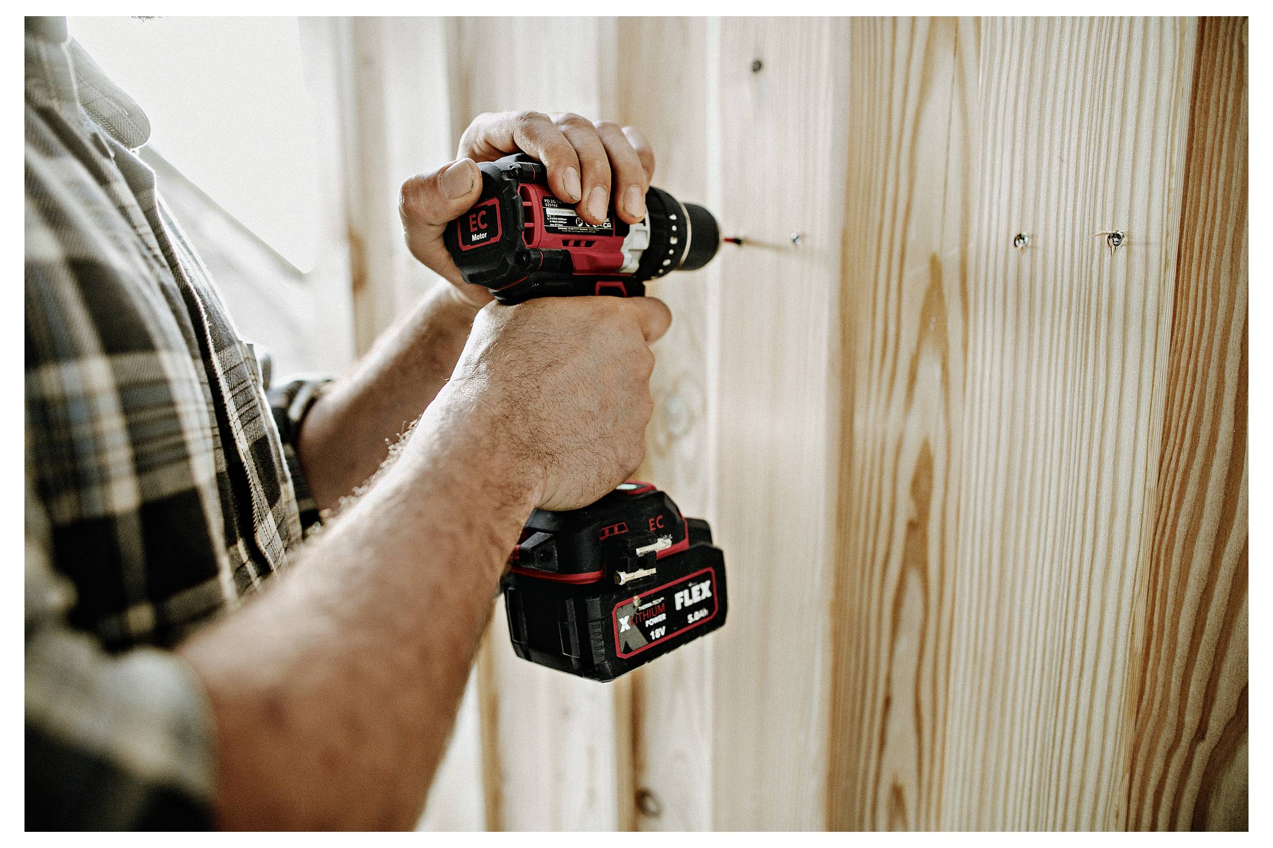 Person using a cordless drill to fasten a screw into a wooden board indoors.