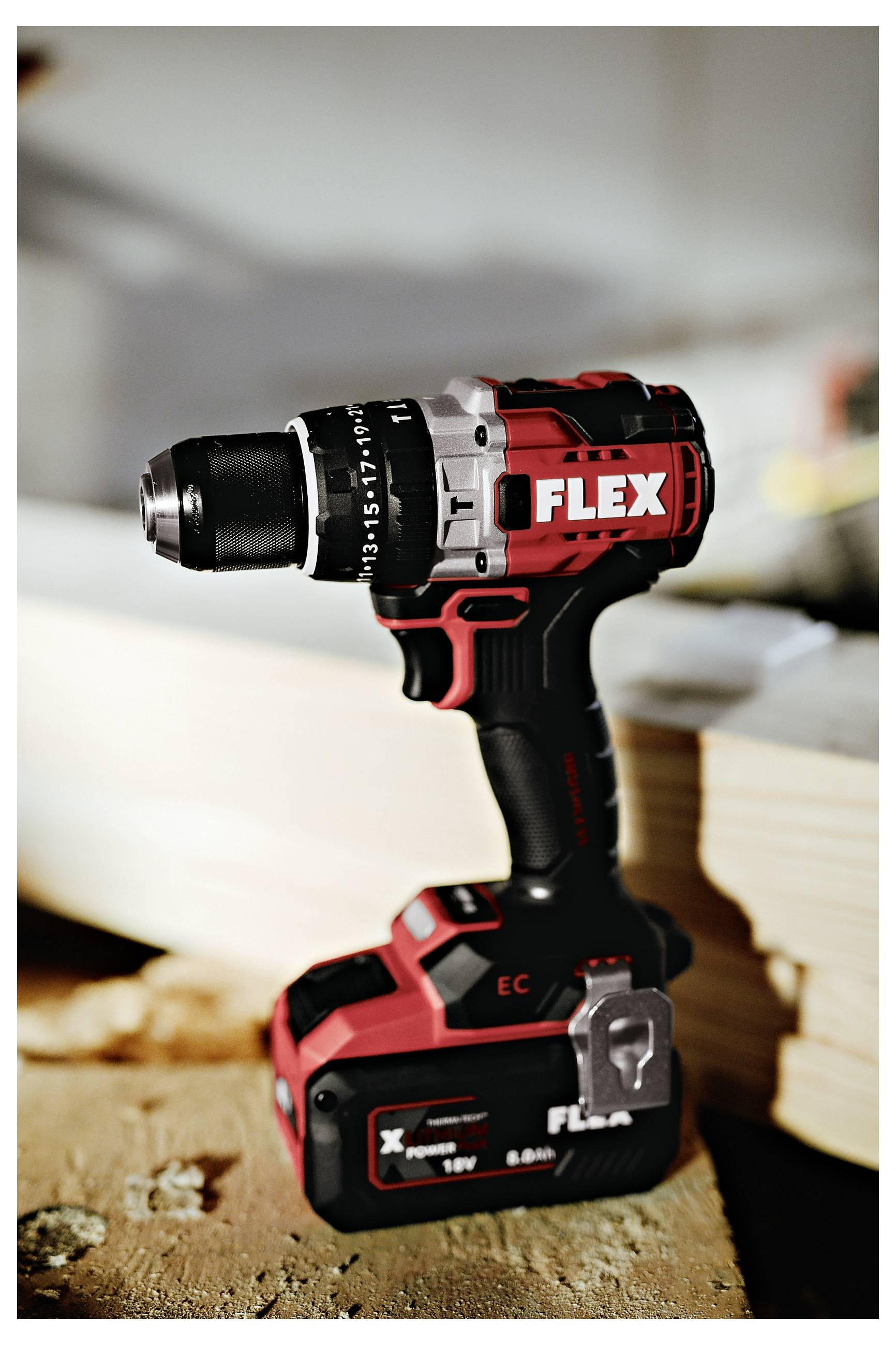 Cordless FLEX drill/driver standing upright on a workbench, with battery attached and a wood bit mounted, in a workshop setting.<br>