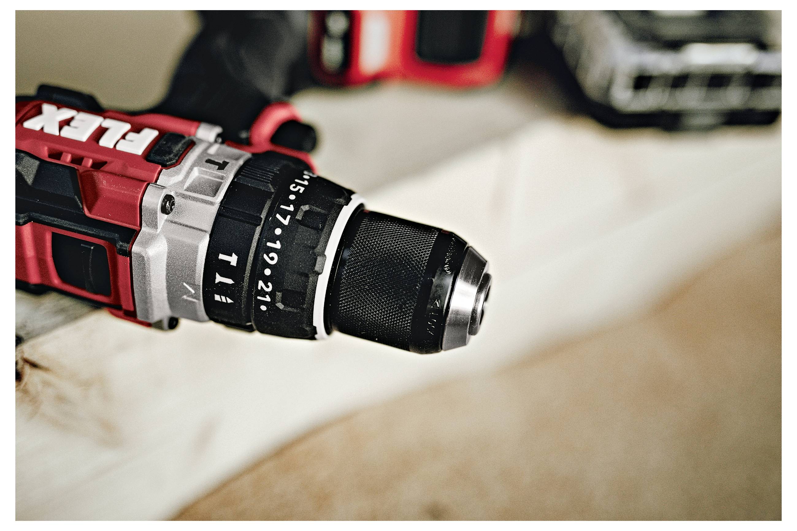 Close-up of a red cordless drill with a black chuck resting on a work surface, with another drill blurred in the background.