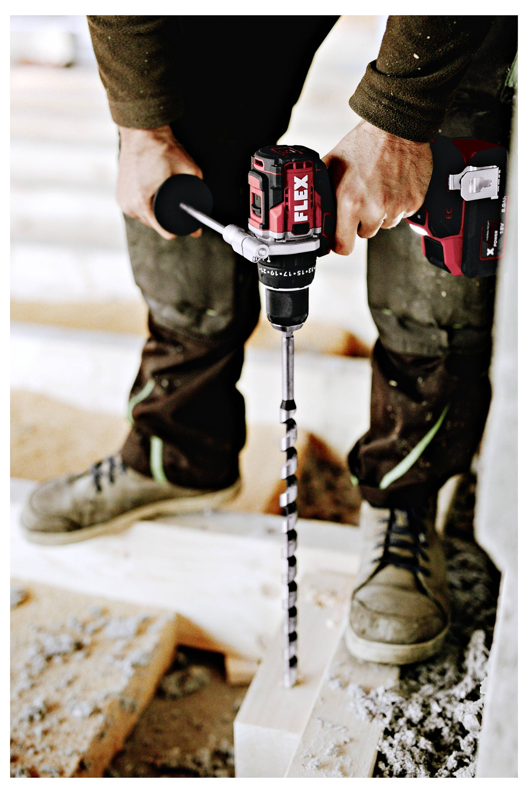 Person using a cordless drill with a long bit to bore a hole into a wooden beam at a construction site<br>
