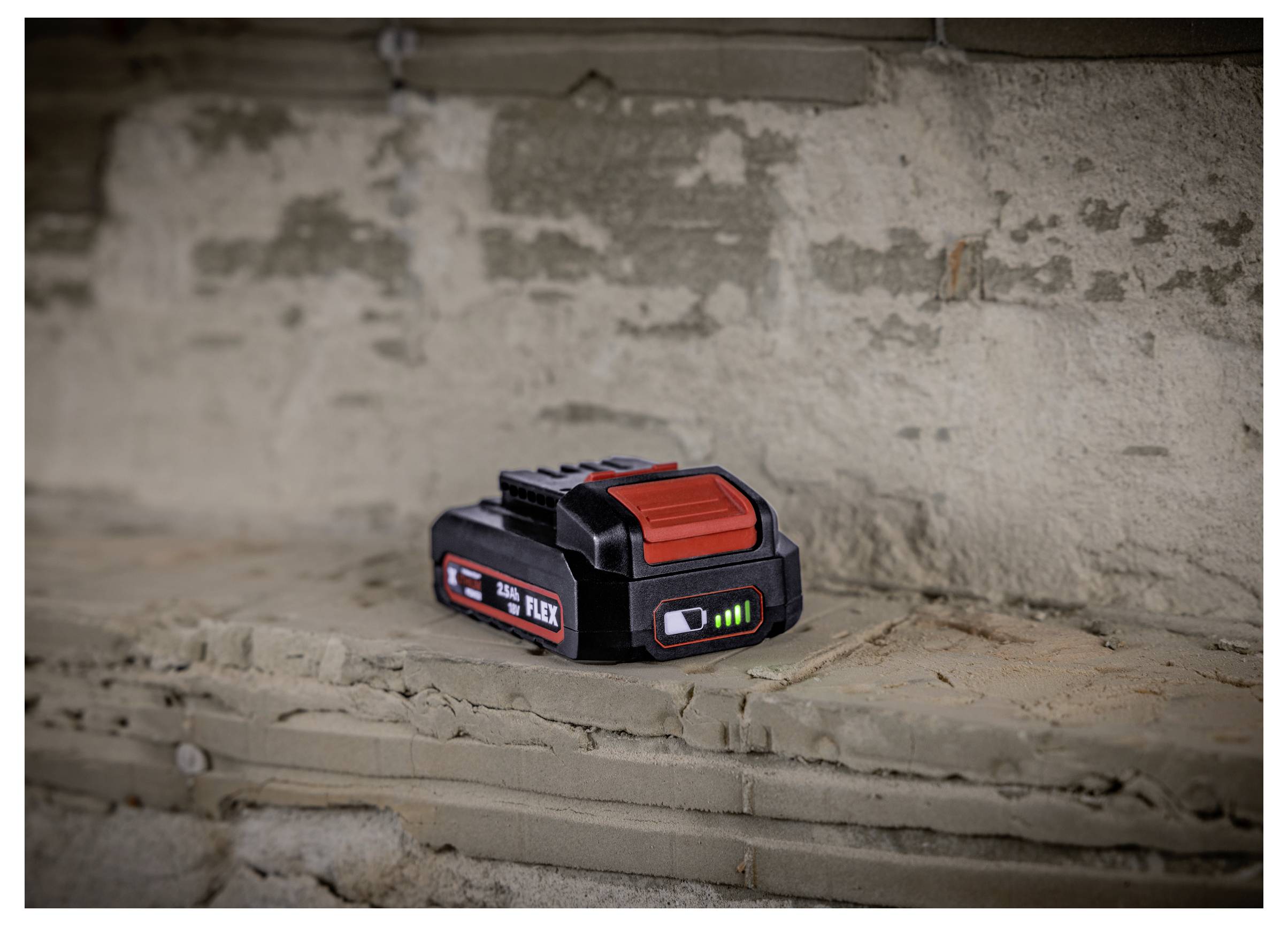 Black-and-red FLEX 24V battery pack resting on a rough concrete ledge, with charge level indicators lit.