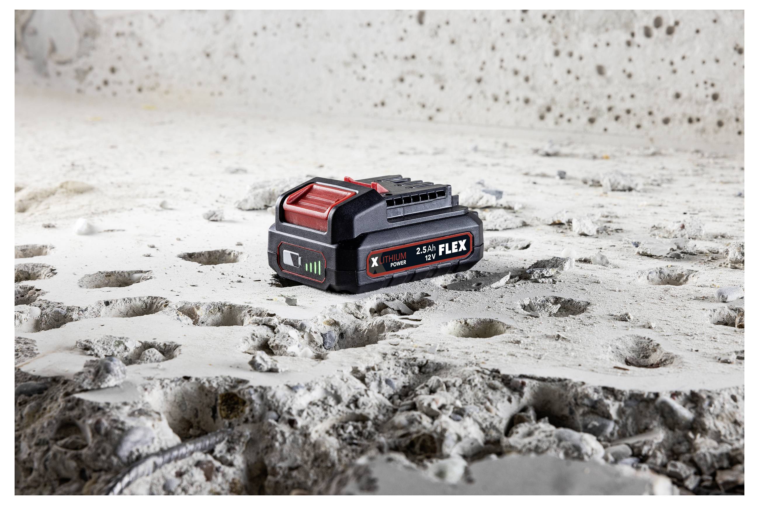 A black and red FLEX 24V battery pack sits on a dusty, rough concrete surface.