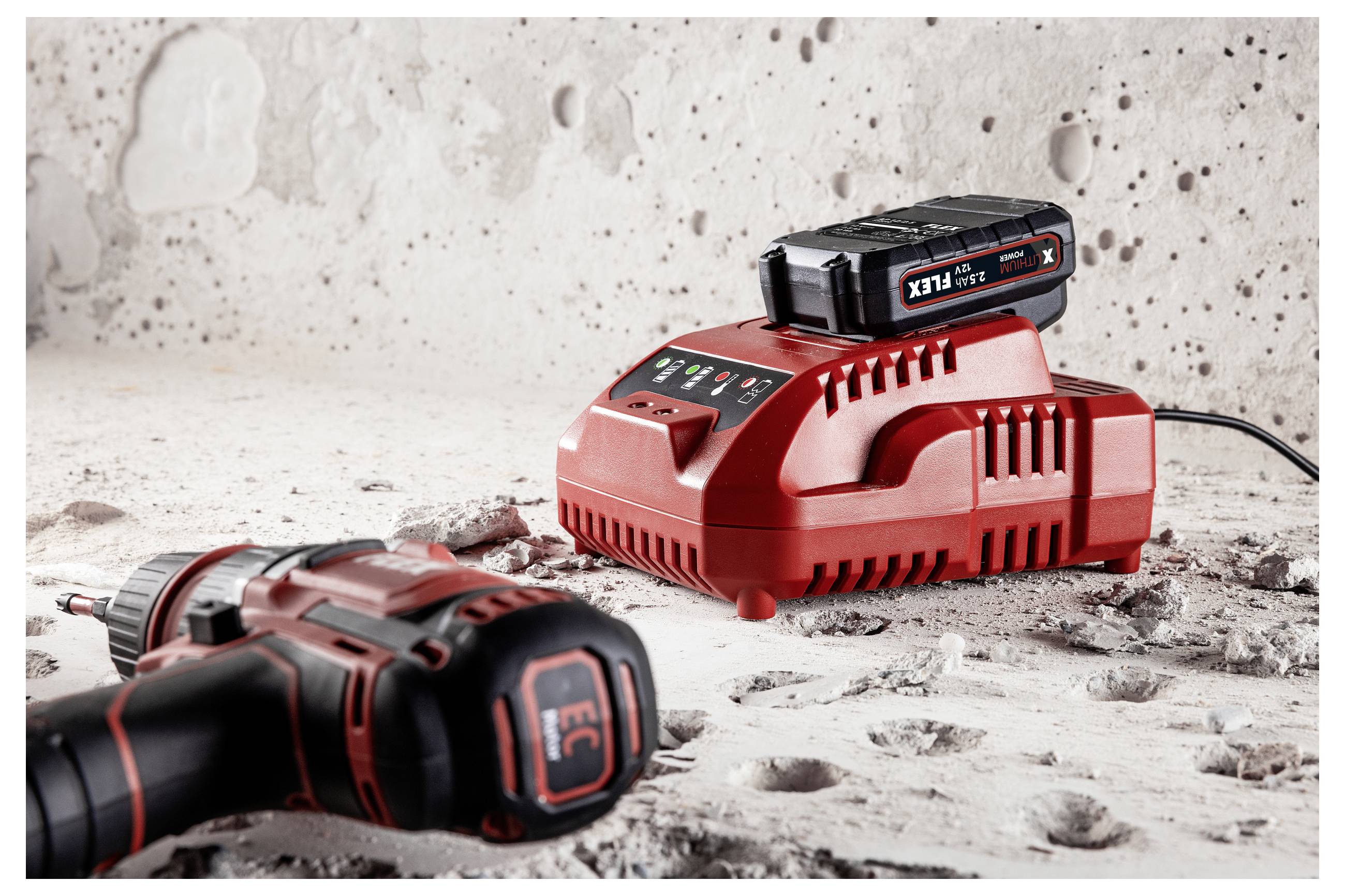Cordless power tool battery charger with battery pack on dusty concrete, and a drill in the foreground.