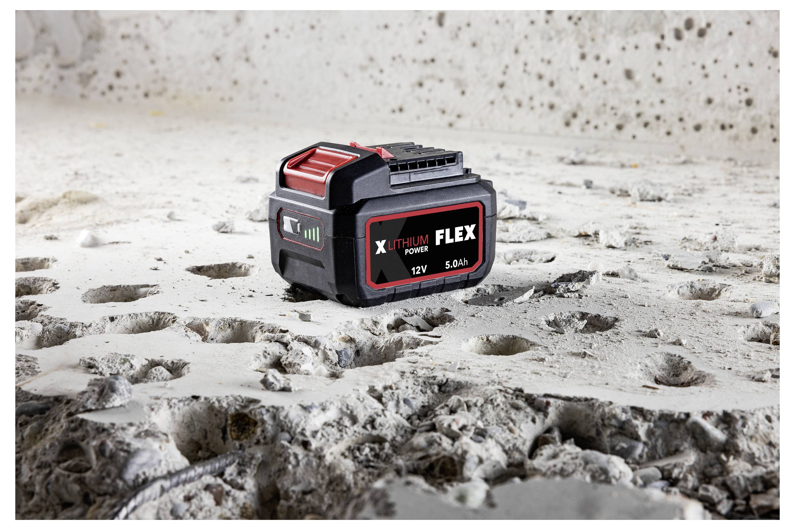 Black and red X-THIUM FLEX 12V 5.0Ah power tool battery sitting on a dusty, worn concrete surface.