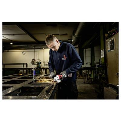 Worker wearing safety gear grinds metal in a workshop, creating sparks while cutting a steel frame.<br>