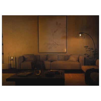 Warmly lit living room with a sofa, floor lamp, coffee table, framed wall art, and candlelight creating a cozy evening atmosphere.