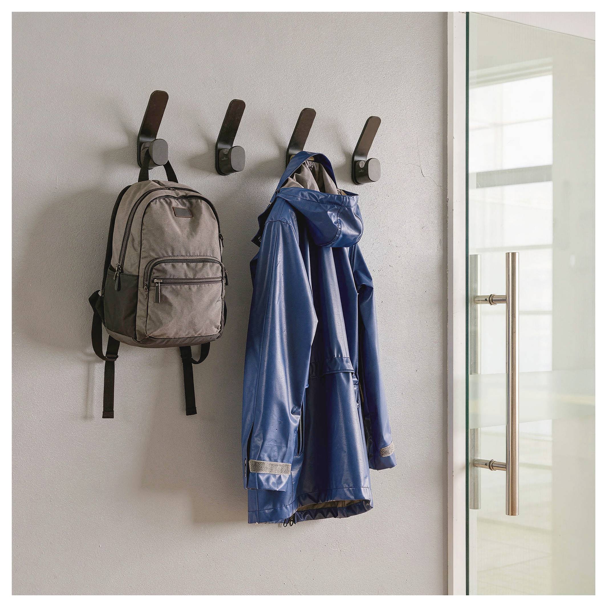 Backpack and blue raincoat hanging on wall hooks beside a glass door.