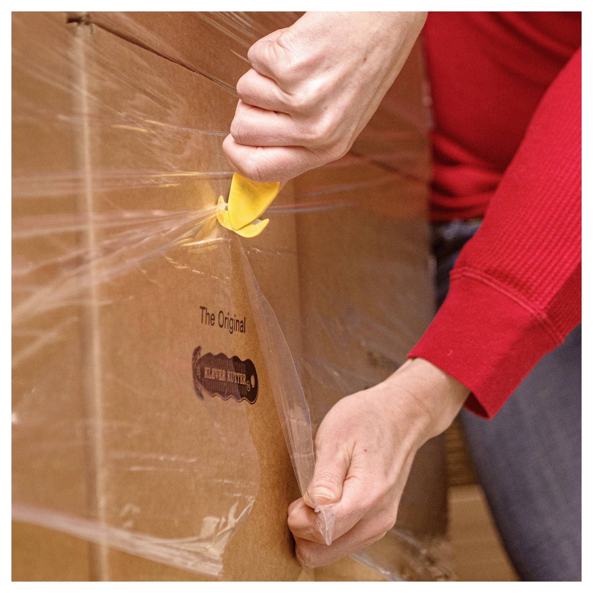 Person uses a yellow cutter to slice open plastic wrap on a large cardboard shipping box.<br>
