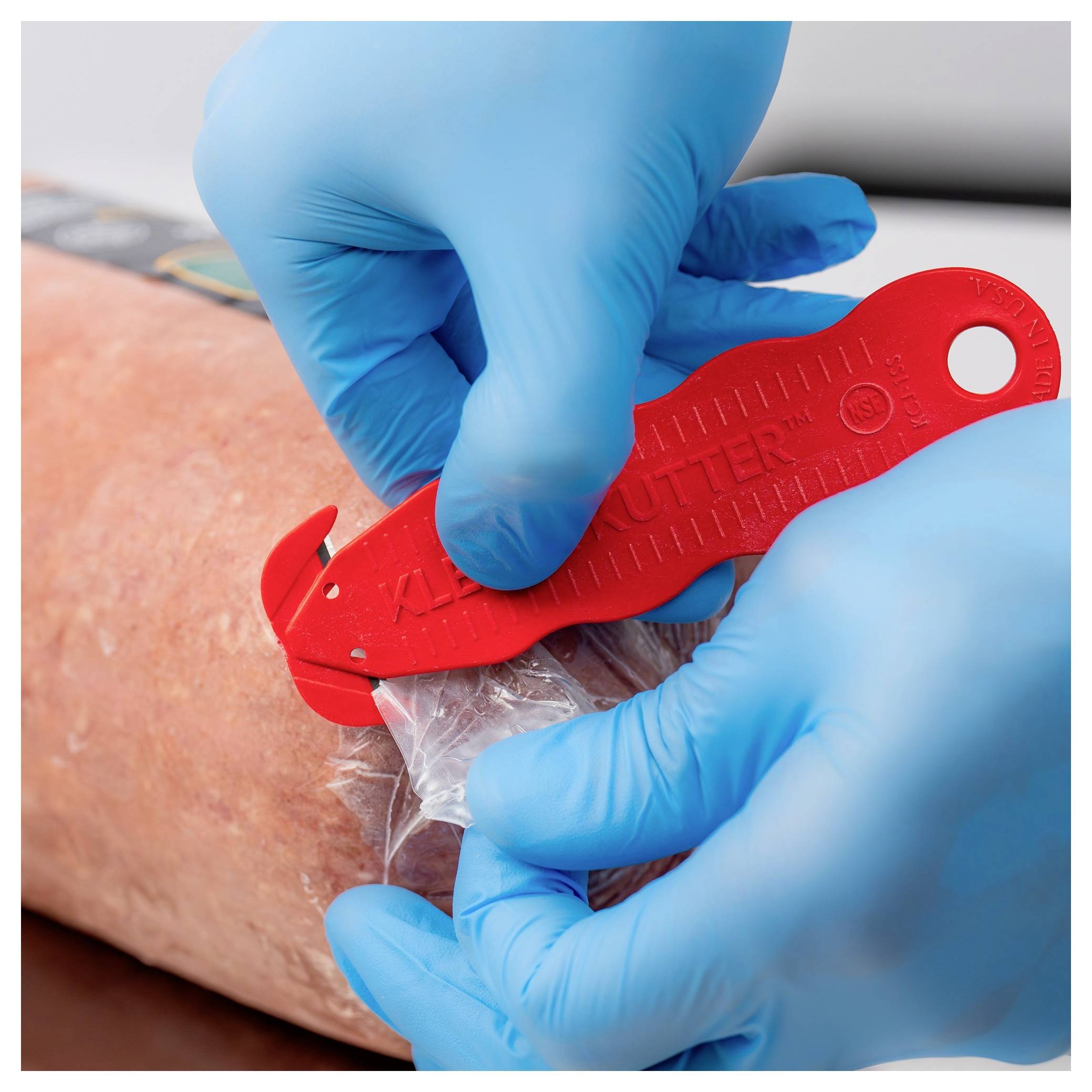 Gloved medical staff cutting plastic wrap from a patient’s arm with a red safety cutter.