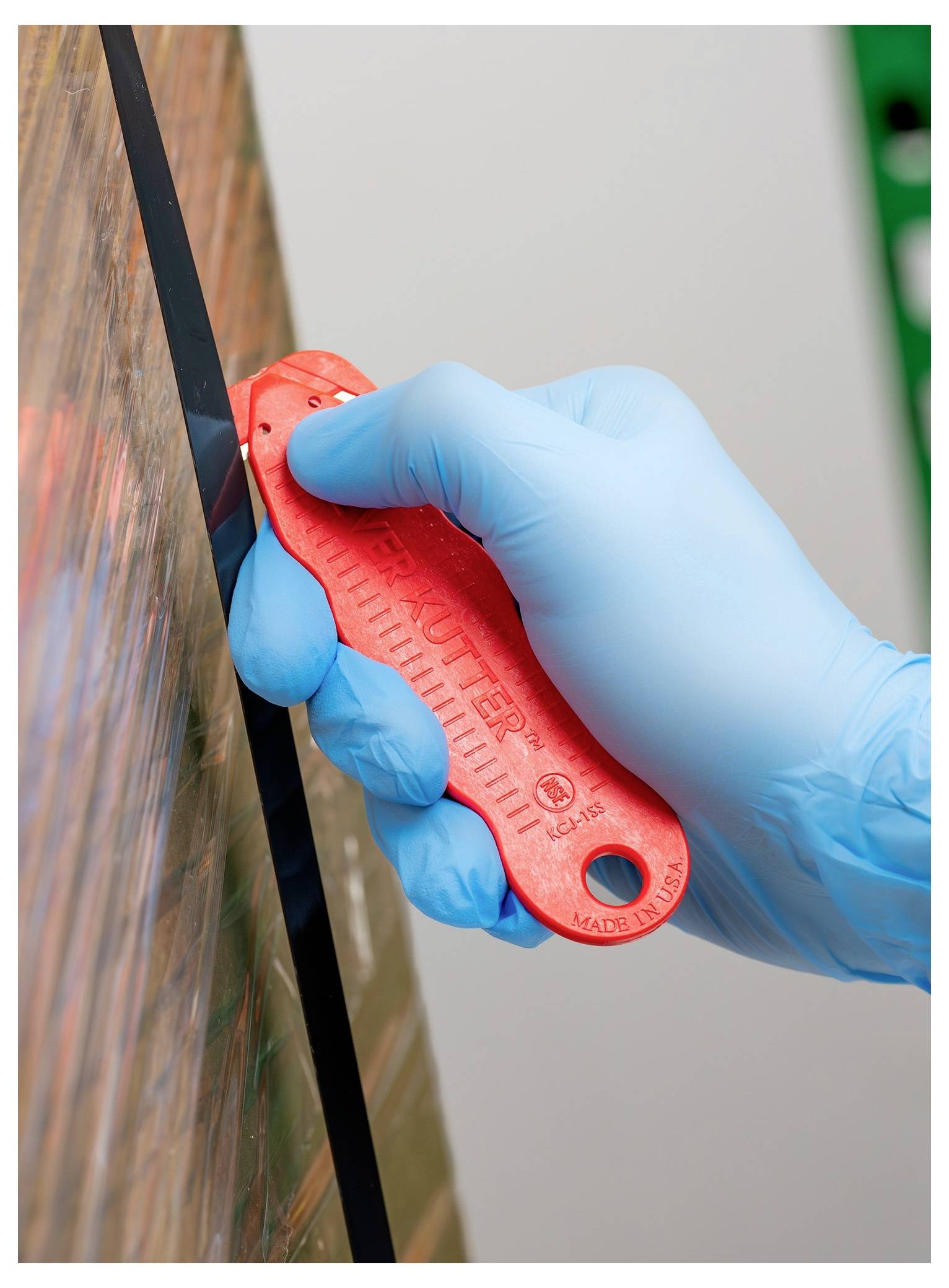 Gloved hand using a red utility knife to cut along the edge of a wooden board<br>