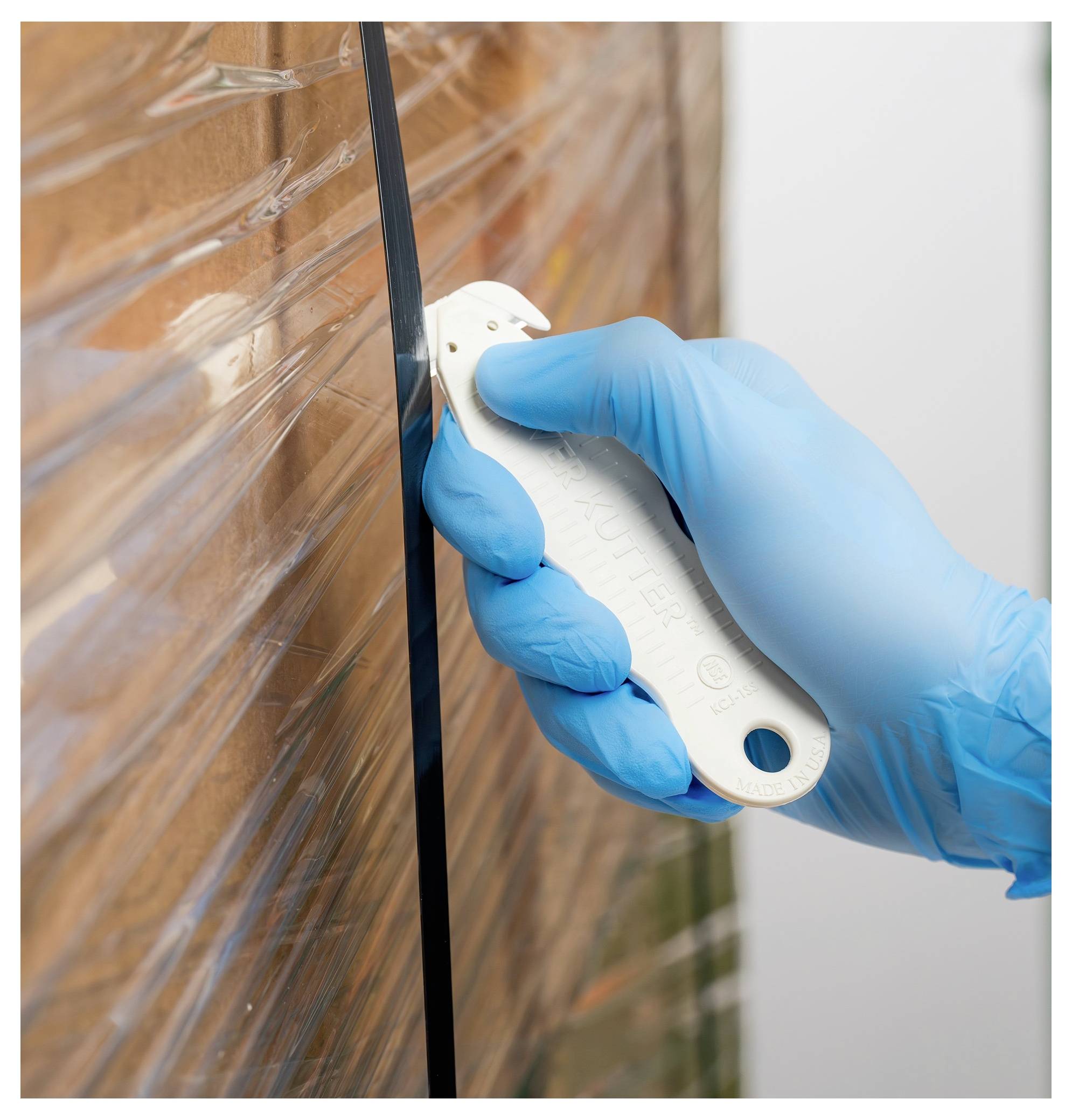 Gloved hand using a utility knife to cut open plastic wrap on a wrapped pallet or package.<br>