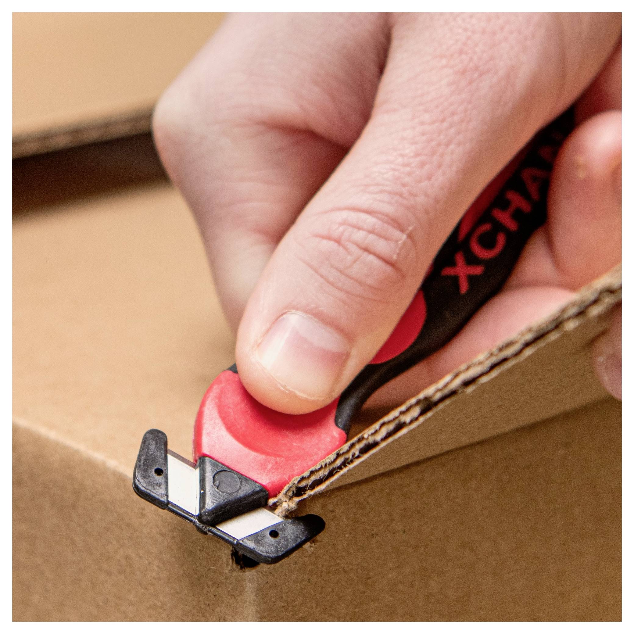 Hand using a red-and-black box cutter to slice open a cardboard shipping box.