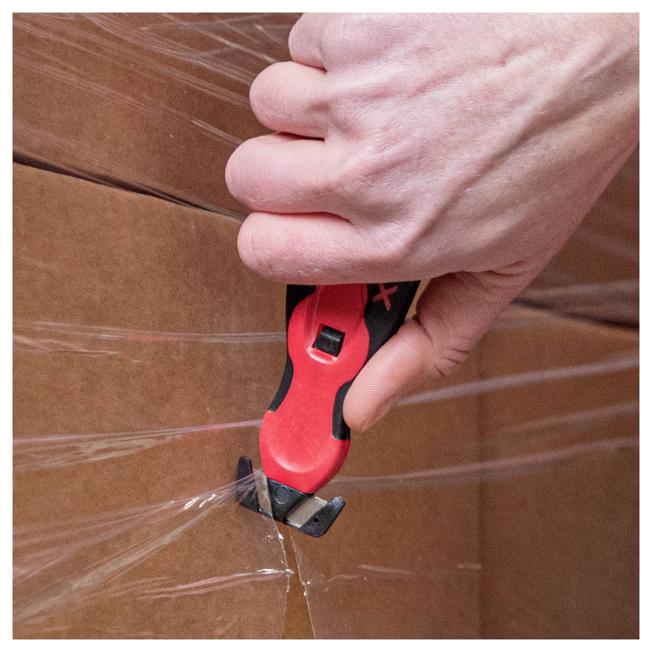 Hand using a red utility knife to cut open a taped cardboard box<br>