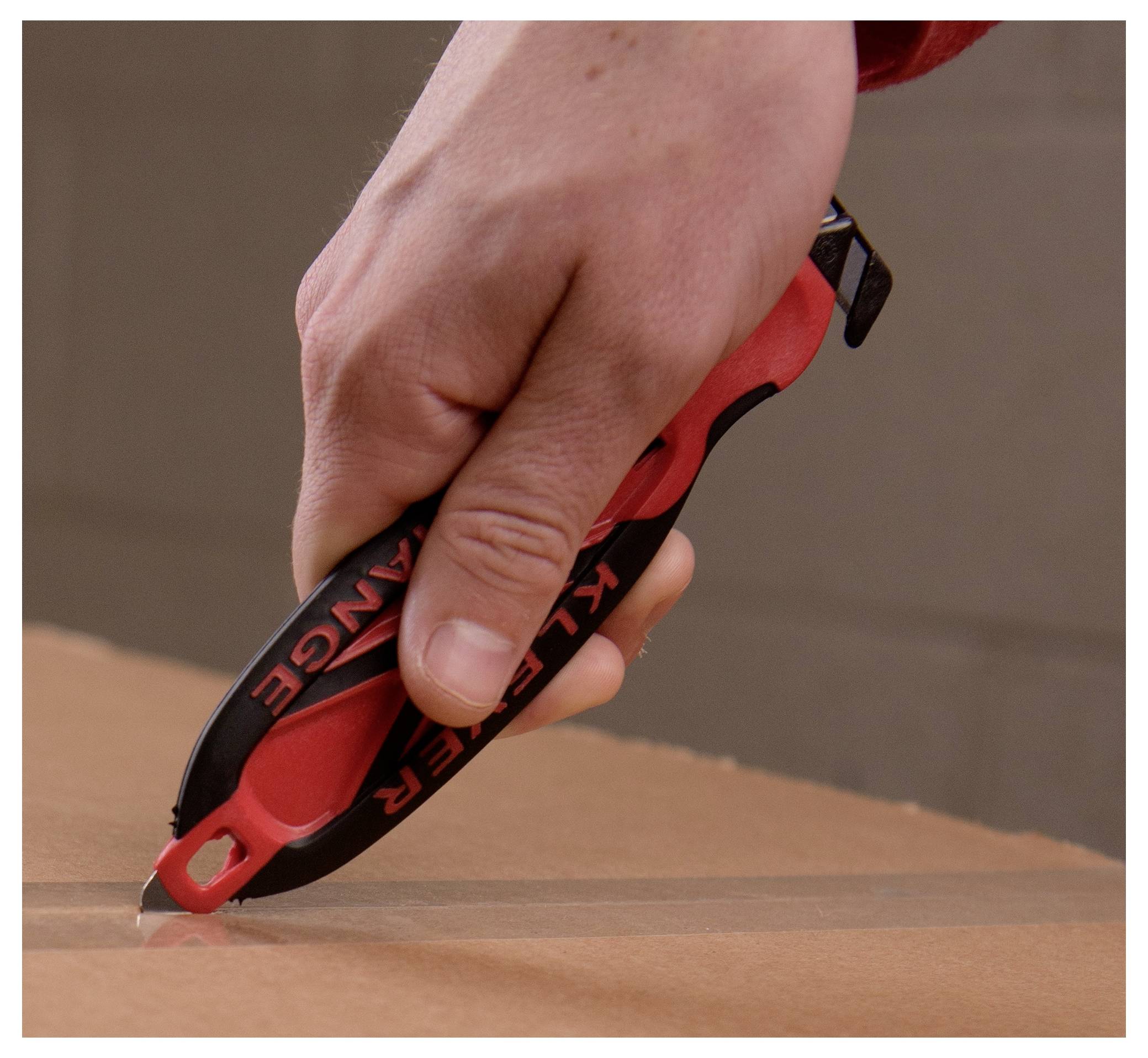 Hand holding a red and black utility knife, cutting into cardboard.