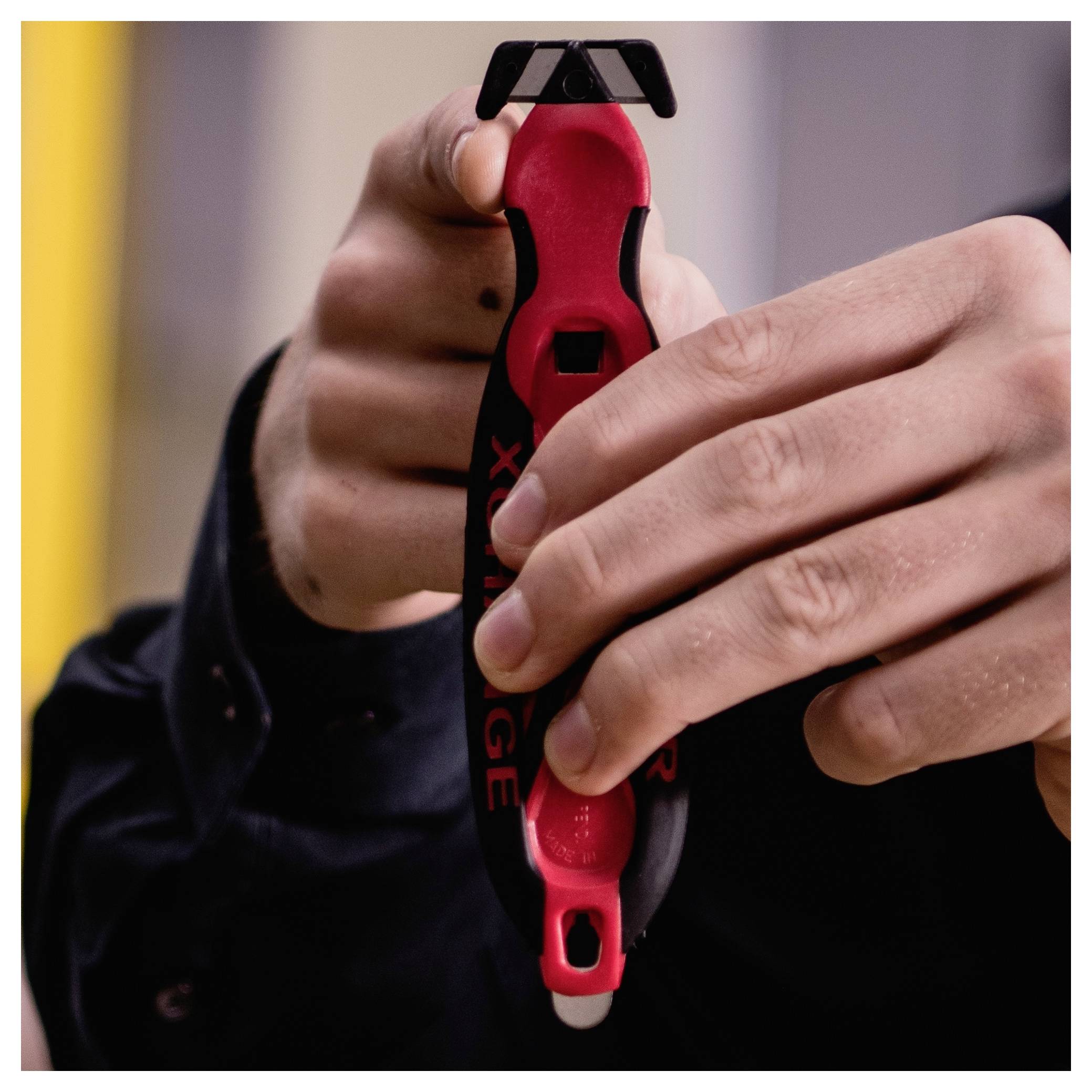 Close-up of hands holding a red-and-black bottle opener, opening a bottle against a blurred indoor background.