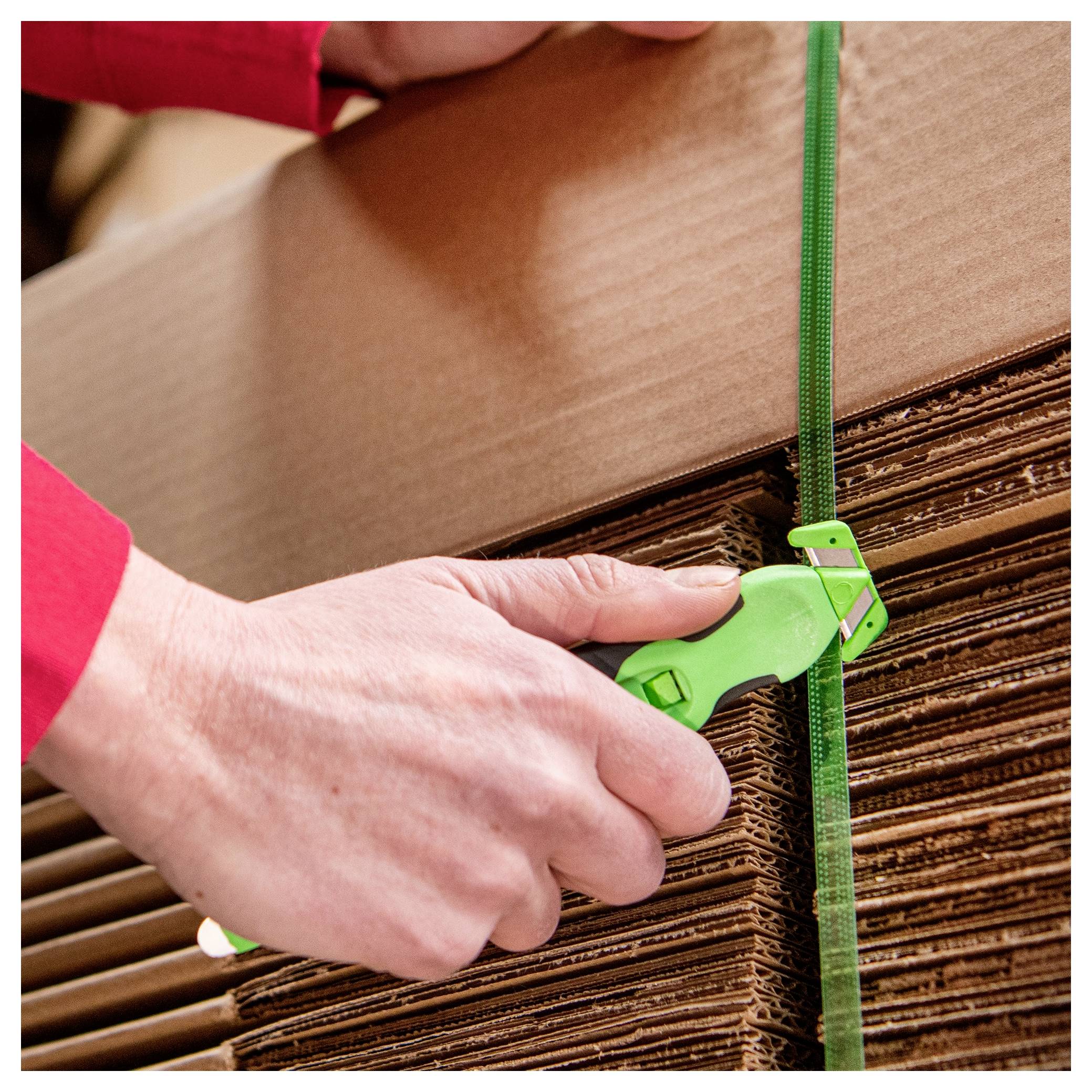 Hands use a green strap tensioner to secure stacked cardboard boxes with packing banding.<br>