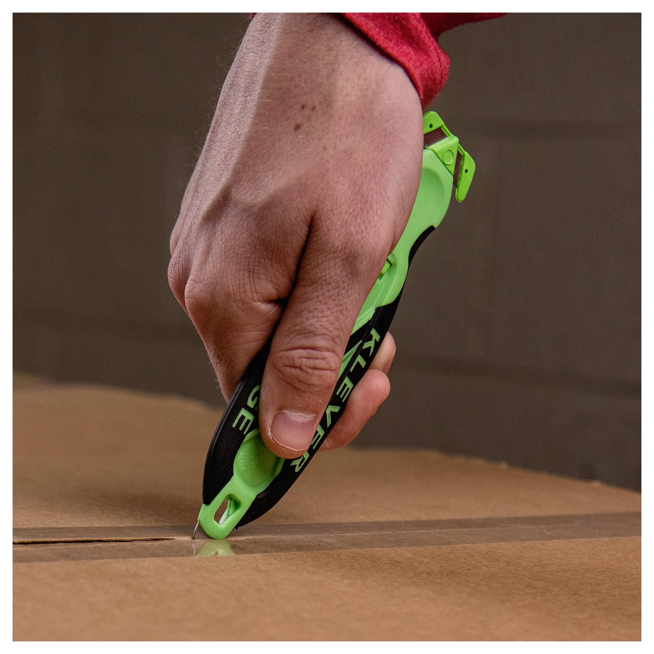 Hand using a green utility knife to cut along the seam of a cardboard box<br>