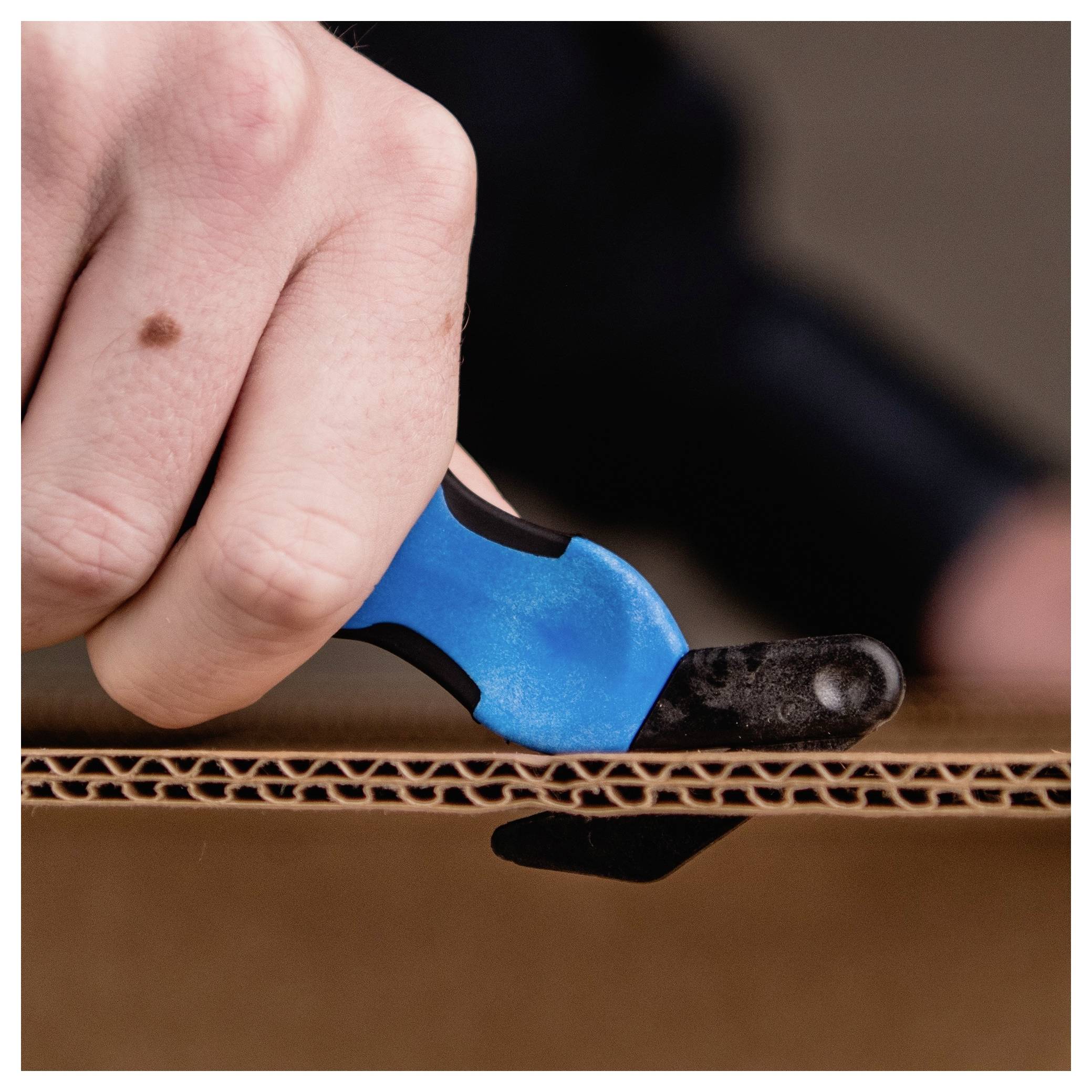 Close-up of a hand using a blue-and-black utility knife to cut along the edge of corrugated cardboard.