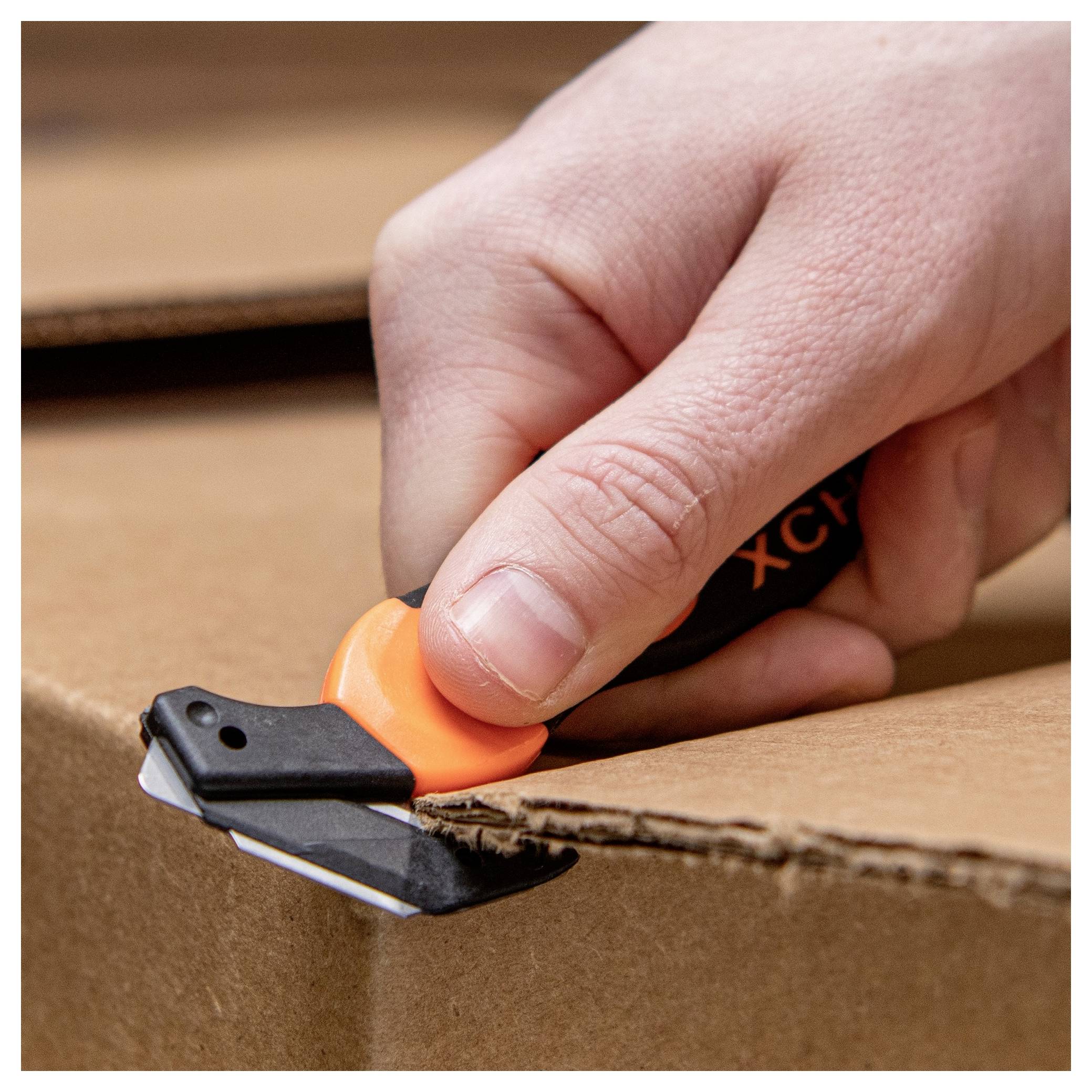 Close-up of a hand using a box cutter to slice open a cardboard box edge.<br>