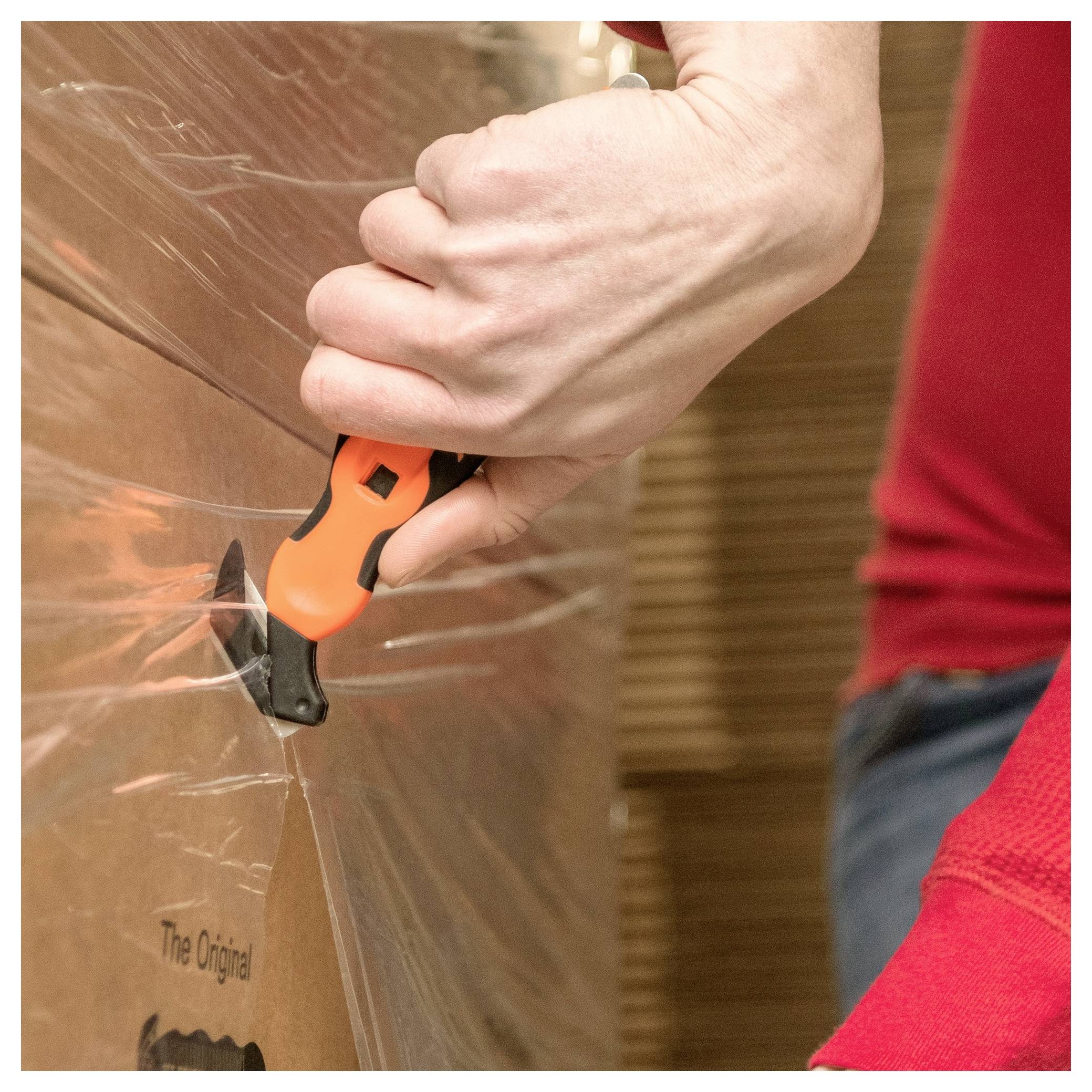 Close-up of a person using a utility knife to cut open plastic wrap on a cardboard box.