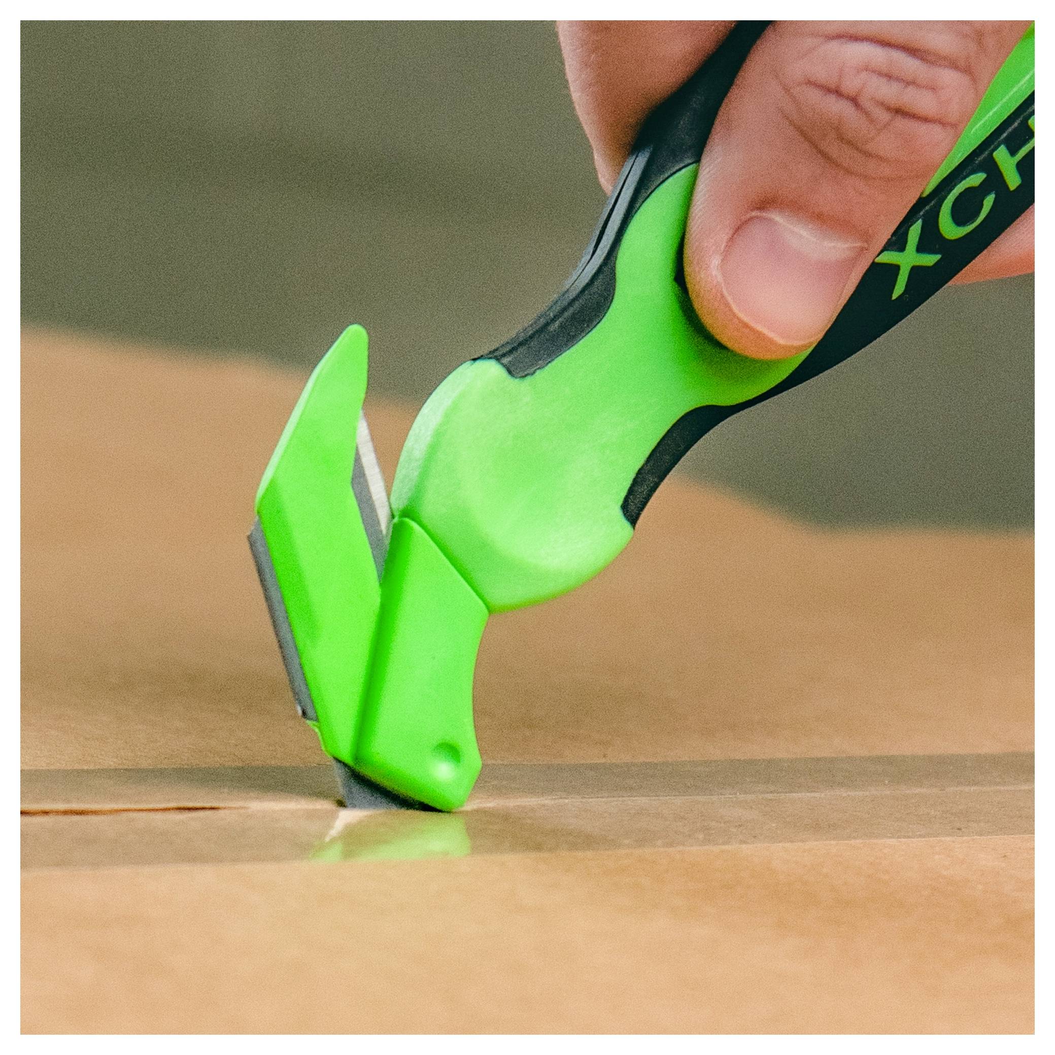 Close-up of a hand using a green utility knife to cut open cardboard.